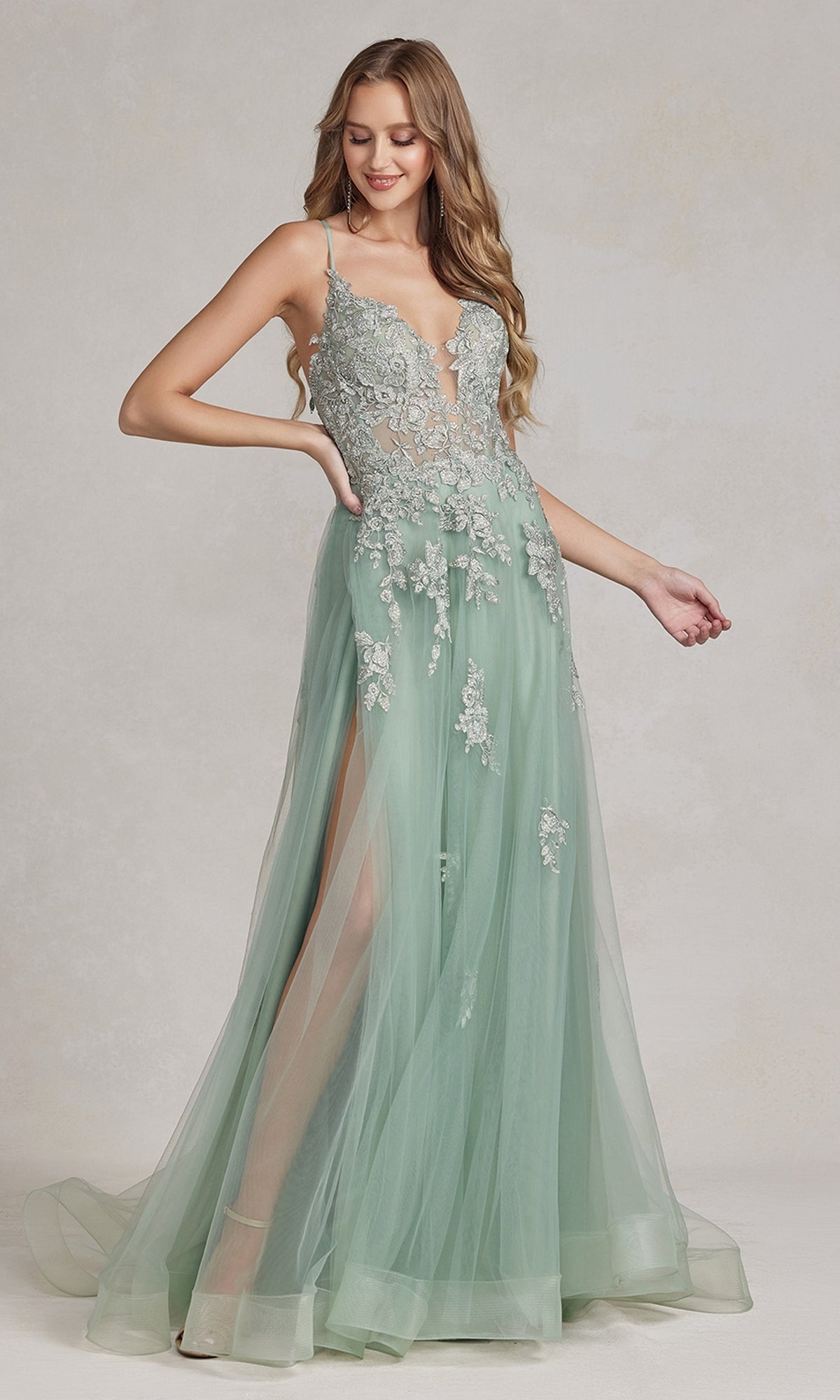 A woman wears the Open-Back Long Prom Ball Gown with Beads, a light green floor-length A-line dress with floral lace details, tulle overlay, beaded appliques, thigh-high slit, and thin shoulder straps.